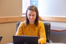 A woman in a yellow sweater smiles while typing on a laptop as she researches best jobs for the future.